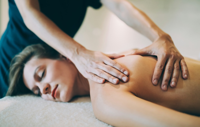 Person receiving a relaxing massage at a spa, hands applying pressure to upper back.